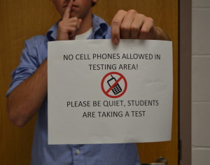 A student poses with a sign prohibiting technology in a testing room.