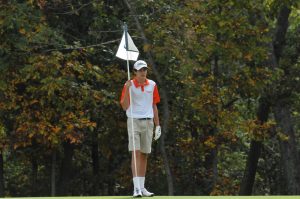 Freshman Cole Kirchner politely holds the flag while players from competing schools are putting. 