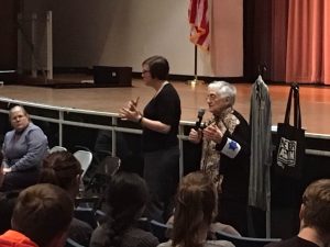 Holocaust survivor Edith Lowy (right) speaks to RHS students Feb. 23. She is wearing a replica of the Star of David armband she was forced to wear in the Wieliczka ghetto. To her right are a replica of a concentration camp prisoner's outfit and a tote bag from the United States Holocaust Memorial Museum that reads "Never Again."